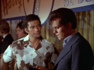 Ben, a Samoan man with brown hair wearing a brown and white aloha shirt, and Steve, a white man with brown hair wearing a blue suit, looking serious.