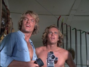 Perry King and Nicholas Hammond as the McDivitt brothers are looking in awe and happiness beyond the camera. Both are young white men with longer, blond hair. Perry is wearing a blue button down shirt, unbuttoned, and Nicholas is shirtless.
