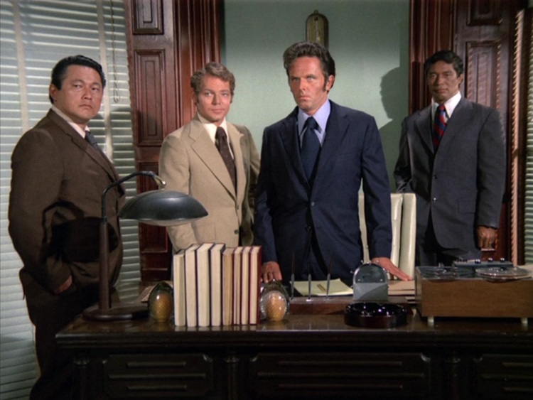 Five-O imposters. Fake Chin is a mid-thirties Asian man; Fake Danny is James MacArthur with his blond, curly hair parted on one side; Fake Steve is a mid-thirties white man; and Fake Ben is a mid-thirties Pacific Islander. They're standing behind a desk in a recreated Five-O office.