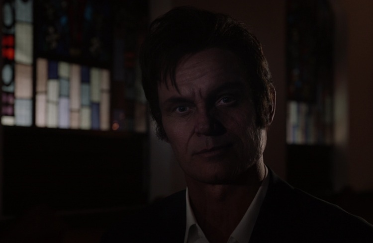 Incredibly dark picture of a CGI Jack Lord, a middle aged white man with dark hair, in a hospital chapel.