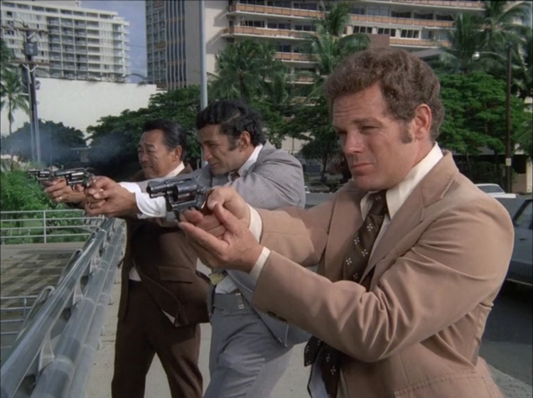 Kam Fong as Chin, an older Asian man with black hair wearing a brown suit, Al Harrington as Ben, a young Pacific Island man with black hair wearing a grey suit, and James MacArthur as Danno, a young white man with dark blond hair wearing a tan suit. The three of them are shooting from the side of a bridge.